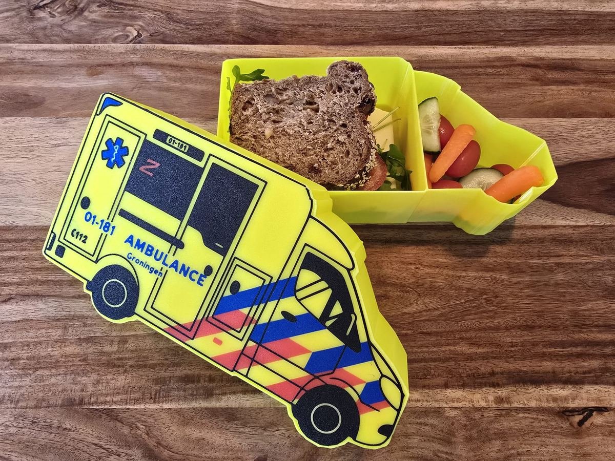 Geopende 3D-geprinte ambulance-lunchbox met een boterham en groenten